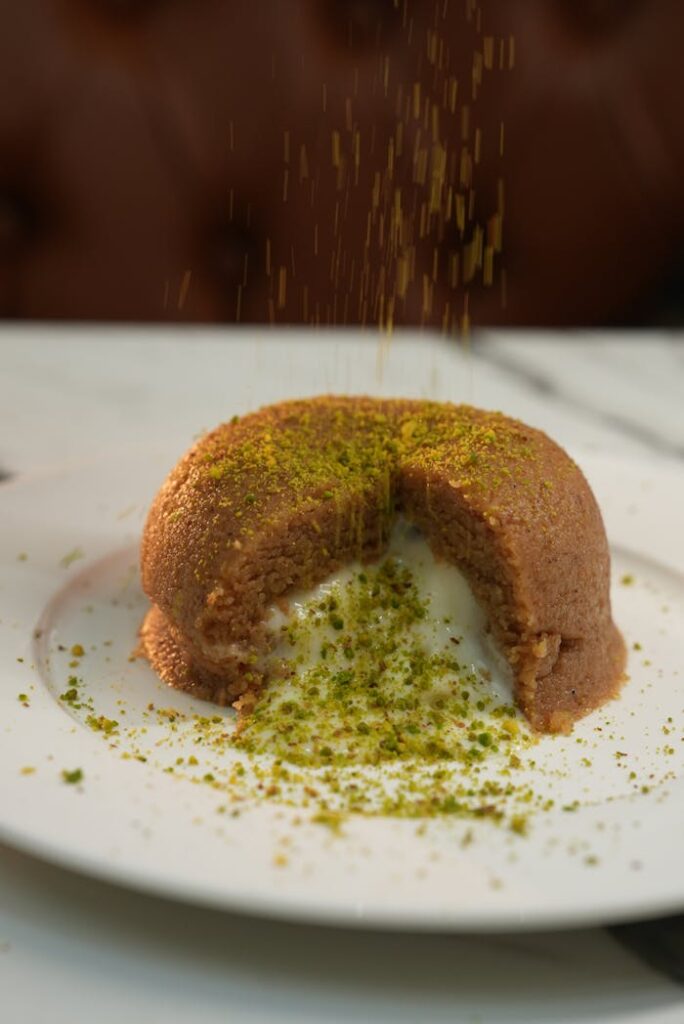 Close-up of melted Turkish semolina halva topped with pistachios, served on a white plate.